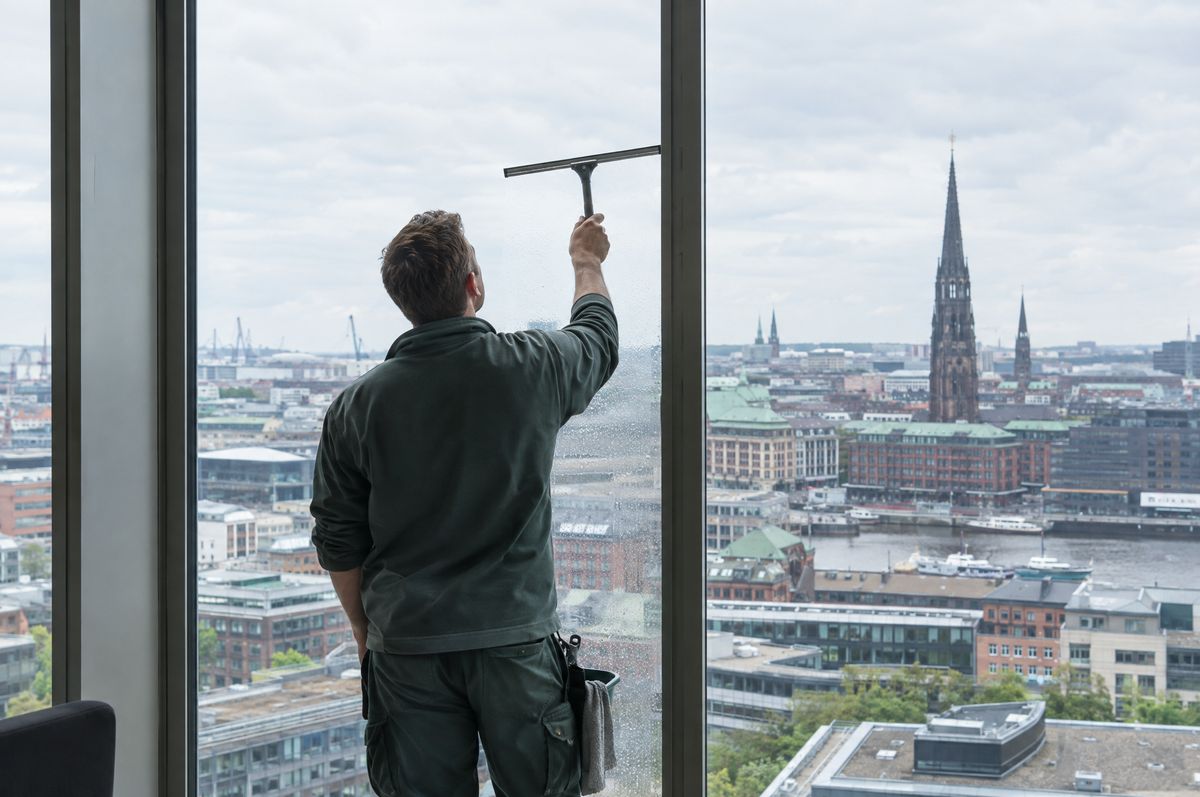Glasreiniger zieht eine raumhohe Fensterscheibe mit Blick über die Dächer Hamburgs ab